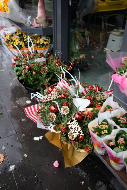 A collection of festive floral arrangements and bouquets displayed outside a flower shop, featuring a variety of flowers including pink roses, white chrysanthemums, and small yellow blooms, all wrappe