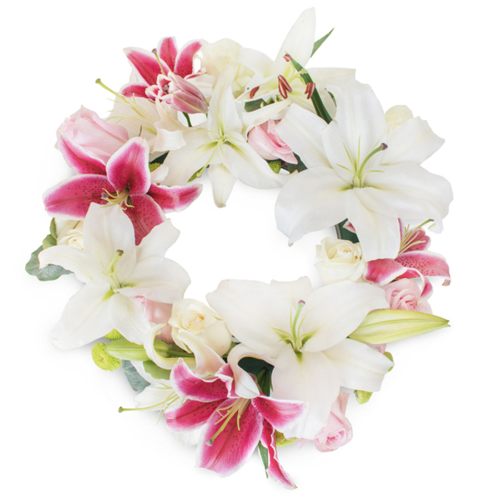 Dominating the scene is a sumptuous memorial wreath, beautifully crafted with the expertise one would expect from trusted Stroud Green florists. Set against a flawless, white background that amplifies its brilliance, the arrangement presents a complete circle of devotion-resplendent in layers of pristine white Oriental lilies and vivid fuchsia-pink, speckled Stargazer lilies. Each white lily opens majestically, revealing elegant green and yellow stamens, their recurved petals reminiscent of classic arrangements found in local ceremonies on Upper Tollington Park or Wray Crescent. Offset perfectly by the glowing cadence of fuchsia lilies, whose magenta tones feature subtle speckles and white-tipped edges, the wreath captures both vibrancy and serenity. Interspersed roses, varying from pearl-cream to pale blush, tumble gently amid the lilies, offering both full blooms and tightly wound buds for a touch of soft, romantic texture. Subtle shades of fresh, muted eucalyptus and other greenery provide balance, glimpsing through the flowerwork with hints of structured depth and natural grace. The whole wreath forms an unbroken, lush circle-symbolizing eternity and remembrance. Perfect for tributes, funeral services, or moments of reflection, this arrangement extends a gentle, enduring message of support, especially when delivered across Stroud Green and its welcoming community.